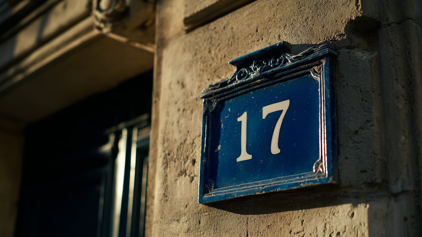 Plaque de rue parisienne ancienne en émail bleu profond avec le numéro 17 stylisé en blanc, fixée sur un mur de pierre claire patinée, lumière naturelle douce de fin d'après-midi mettant en valeur le grain de la pierre et les reflets de l'émail